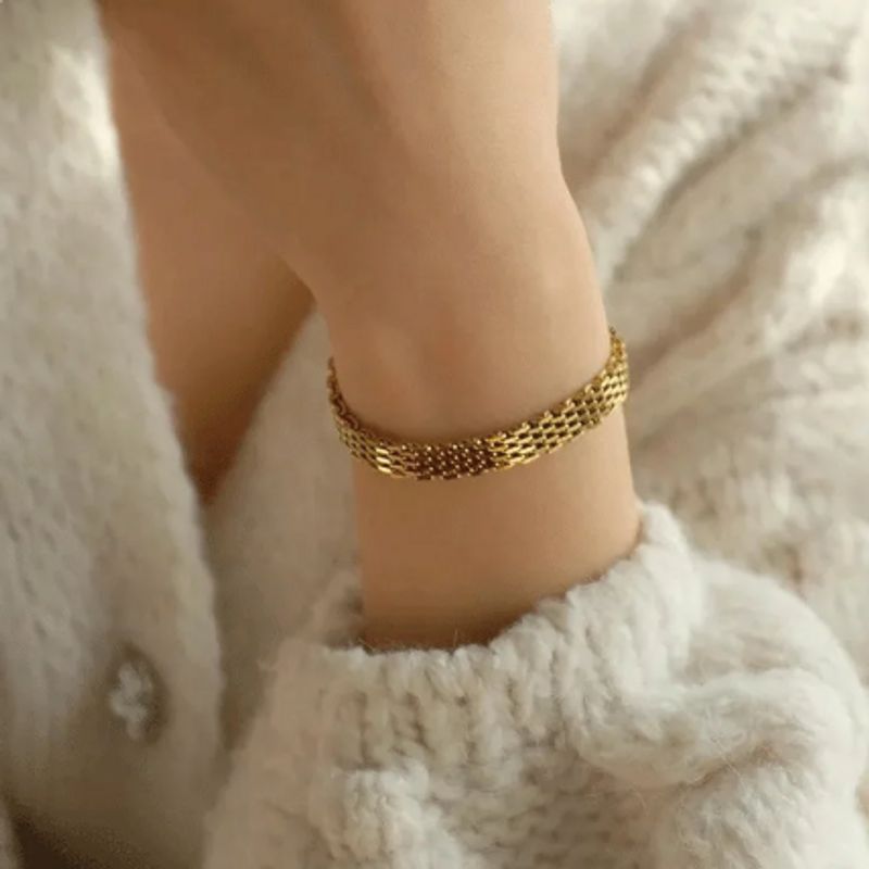 Bracelet à maille résille avec fermoir homard en acier inoxydable sur un poignet de femme chaudement vêtu d'un gros pull blanc en laine - coloris acier plaqué or