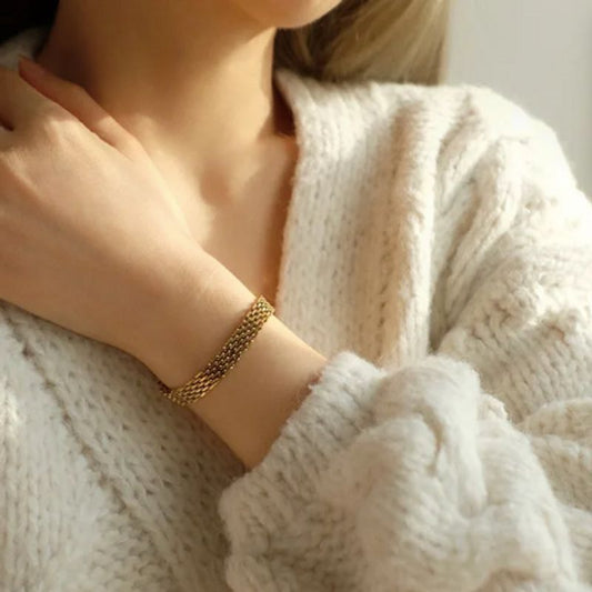 Bracelet à maille résille avec fermoir homard en acier inoxydable sur un poignet de femme chaudement vêtu d'un gros pull blanc en laine - coloris or