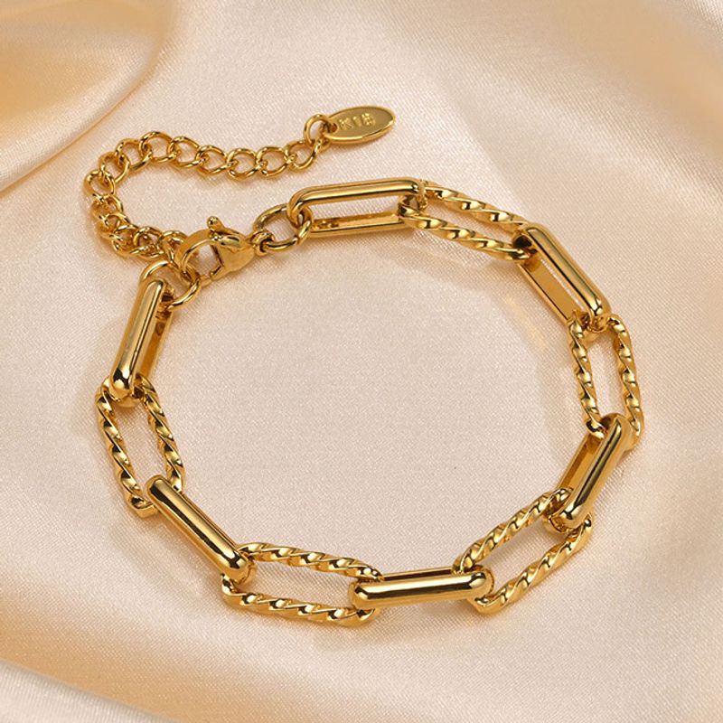 Bracelet à maillons trombones dorés en acier inoxydable plaqué or présenté fermé et à plat sur un tissus satiné de couleur beige crème pour femme