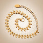 Bracelet à maillons olives dorés en acier inoxydable pour femme - présenté en spirale, façon coquille d'escargot à plat et ouvert sur un fond marron très clair - coloris plaqué or