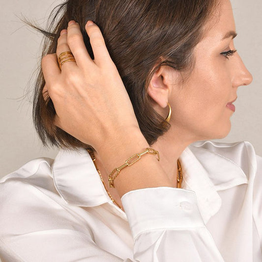 Bracelet à maillons trombones dorés en acier inoxydable plaqué or présenté autour du poignet d'une jolie femme élégante