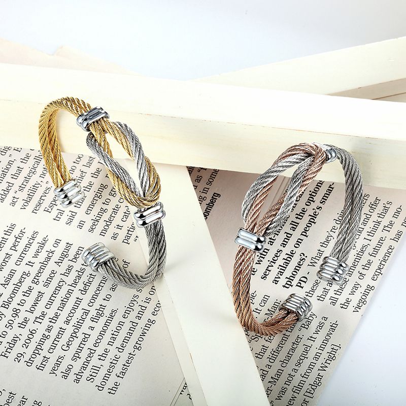 Vue sur deux bracelets manchette à câble formant un nœud de boucles entrelacées en acier inoxydable - deux coloris or et argent - or rose et argent