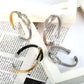 Vue sur quatre bracelets manchette à câble formant un nœud de boucles entrelacées en acier inoxydable - Jonc ouvert - quatre coloris disponibles