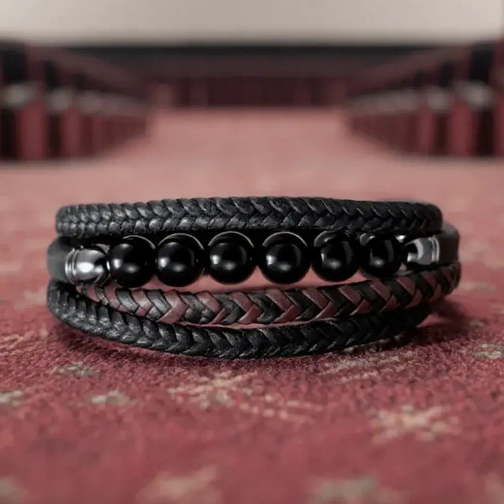 Plan large sur le bracelet Oris dévoilant la lanière tressée bicolore noir et café. La composition repose avec élégance sur la moquette, offrant un aperçu complet du tressage technique et du fermoir acier.