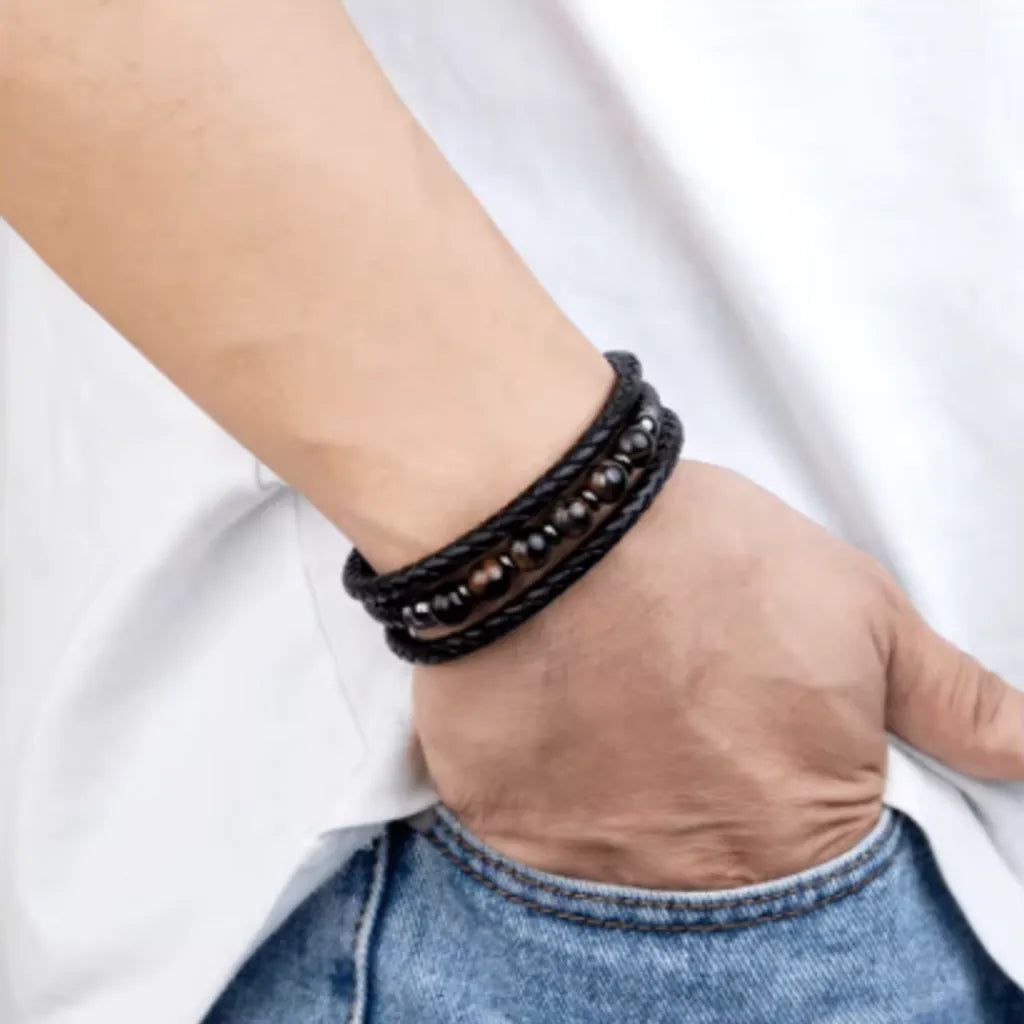 Bracelet multillanière en cuir noir de qualité avec perles oeil de tigre  - porté sur un poignet droit d'un homme, la main enfouie dans la poche de son pantalon en jean - Wrap hypoallergénique.