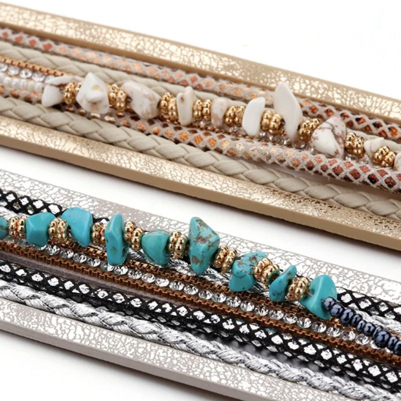 Gros plan sur deux bracelets bohème multilanière pour femme perlés de pierres naturelles bleu et beige, strass cristal, présentation à plat sur un plan de travail blanc.