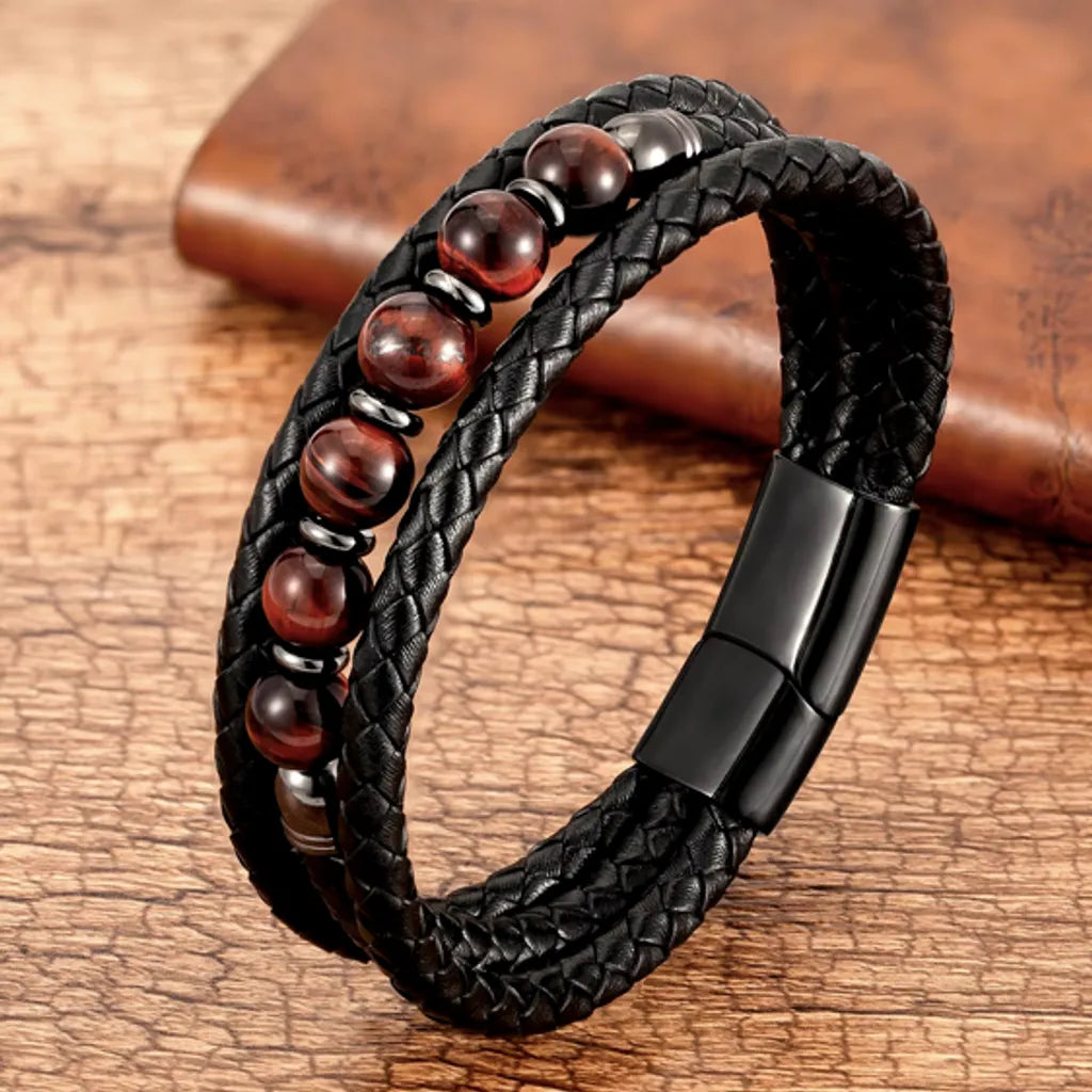 Bracelet en cuir de qualité pour homme avec perles de pierre œil de tigre rouge   posé sur une vieille table rustique en bois clair.