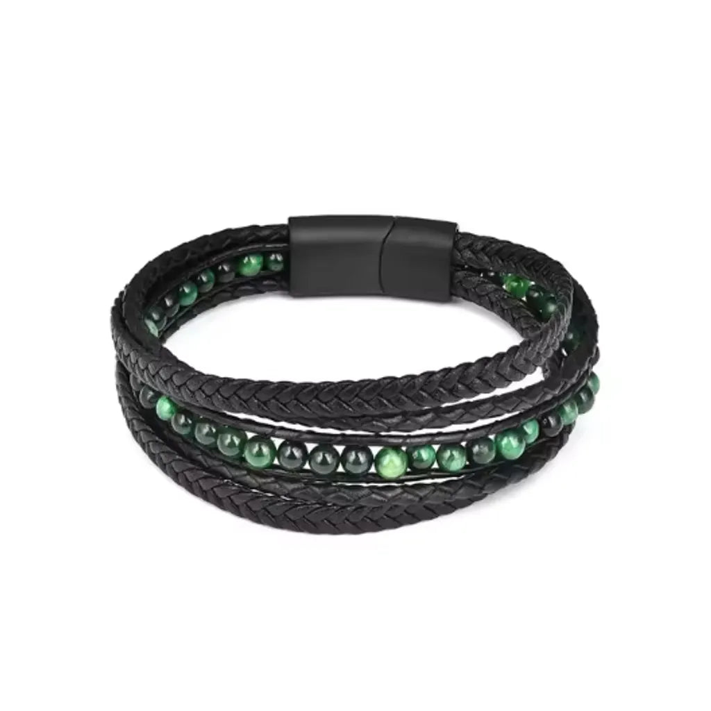 Bracelet multitours en cuir noir tressé, embelli par des perles œil de tigre verte aux reflets chatoyants. Sur un fond blanc clair, cette pièce allie la sophistication des pierres naturelles et la qualité artisanale de son fermoir magnétique noir.