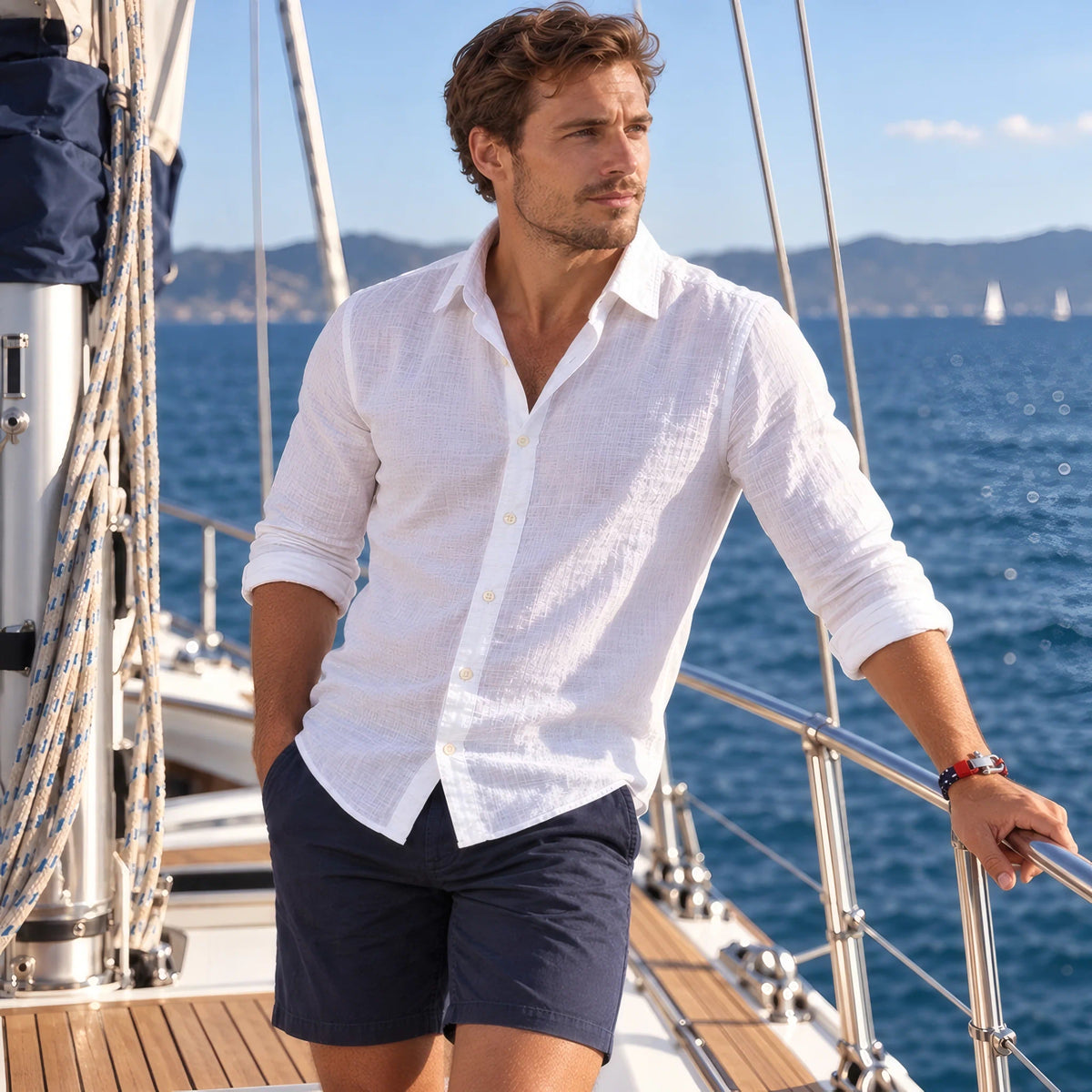 Homme en chemise blanche, main sur le bastingage d'un voilier, portant le bracelet cordon Nautis.