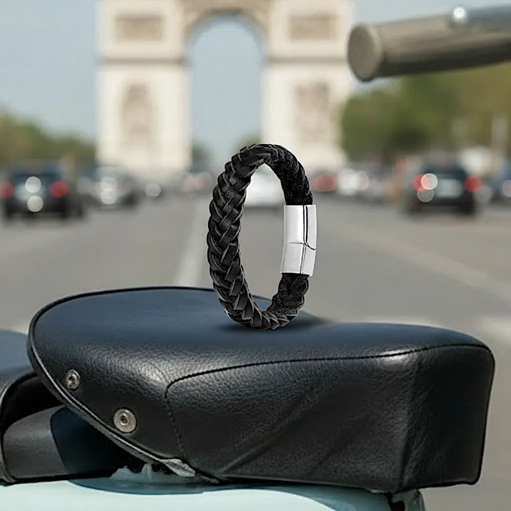 Le bracelet Nero cuir noir tressé en équilibre sur une selle Vespa. Le fermoir magnétique se détache sur le fond urbain des Champs-Élysées.