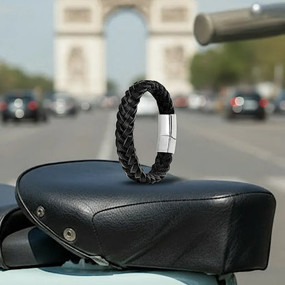 Le bracelet Nero cuir noir tressé en équilibre sur une selle Vespa. Le fermoir magnétique se détache sur le fond urbain des Champs-Élysées.