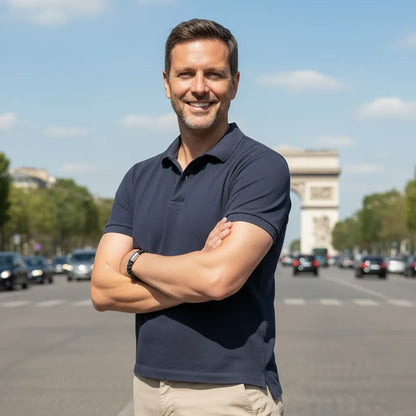 Plan poitrine. L'homme aux bras croisés porte le bracelet Nero en cuir noir tressé sur fond des Champs-Élysées et de l'Arc de Triomphe.