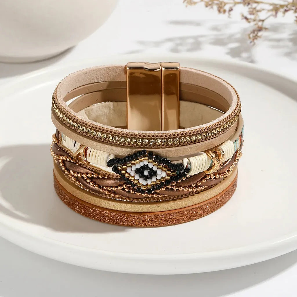 Bracelet Œil du Chaman amérindien multi-rangs en cuir microfibre beige. Ses strass scintillent, posé au centre d'une assiette blanche en porcelaine.