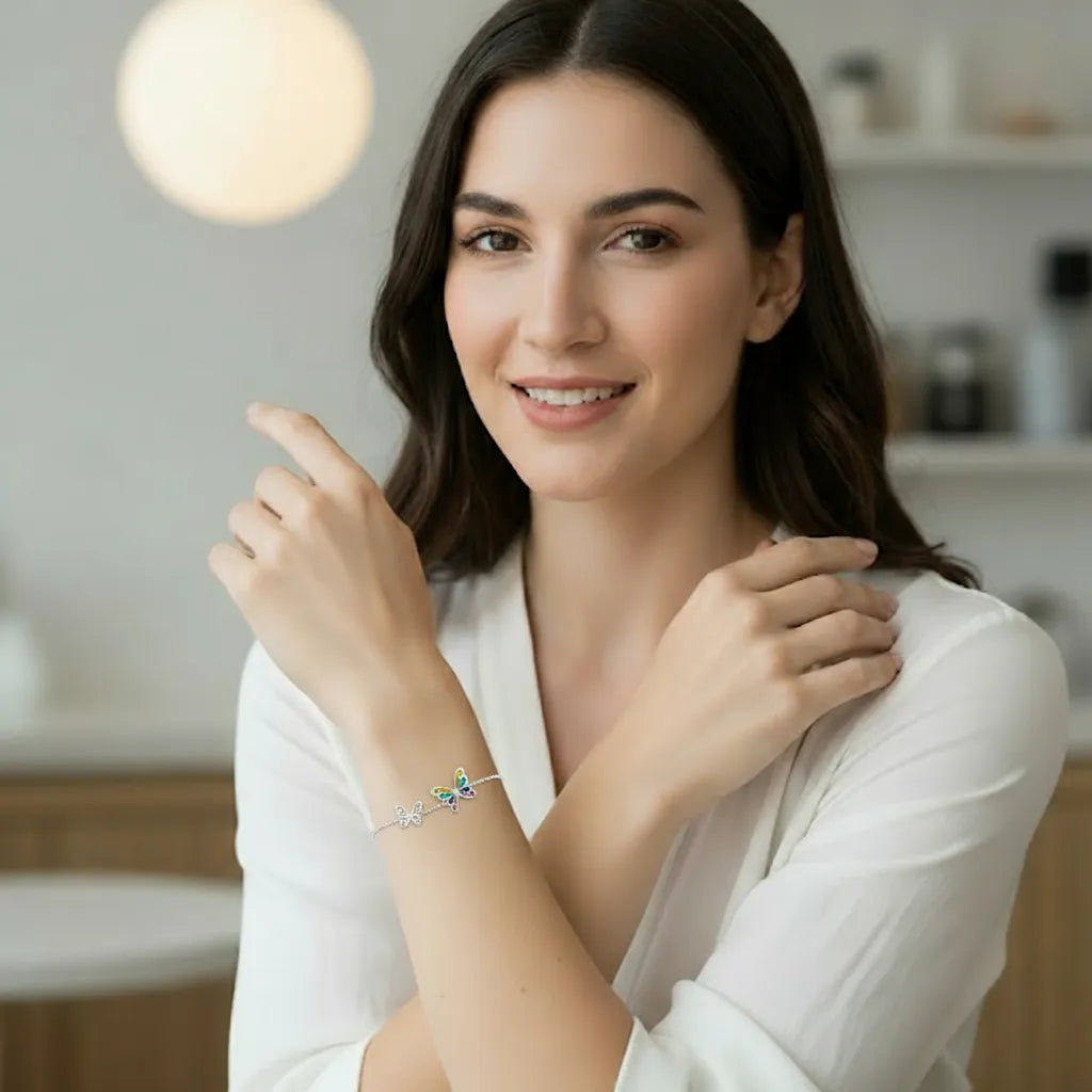 Femme souriante en tenue blanche portant le bracelet Papilla en argent 925, deux papillons délicats se font écho sur son poignet, scène lumineuse dans un appartement raffiné.