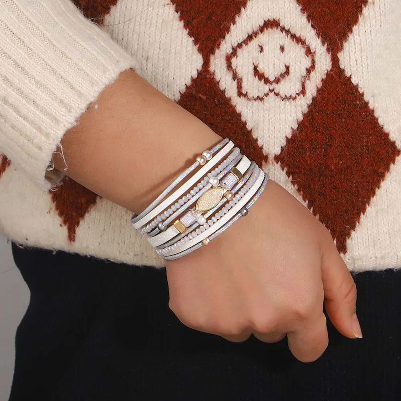 Bracelet Pierre Bohème – wrap porté autour d'un poignet de femme, ce multilanière se présente avec des perles à effet nacrées, des lanières en cuir PU de couleur blanc et un solide fermoir magnétique doré.