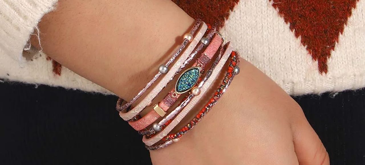 Bracelet pierre bohème avec perles, wrap pour femme en cuir PU de couleur rose présentée autour d'un poignet féminin à la main enfouie dans la poche de son pantalon noir.