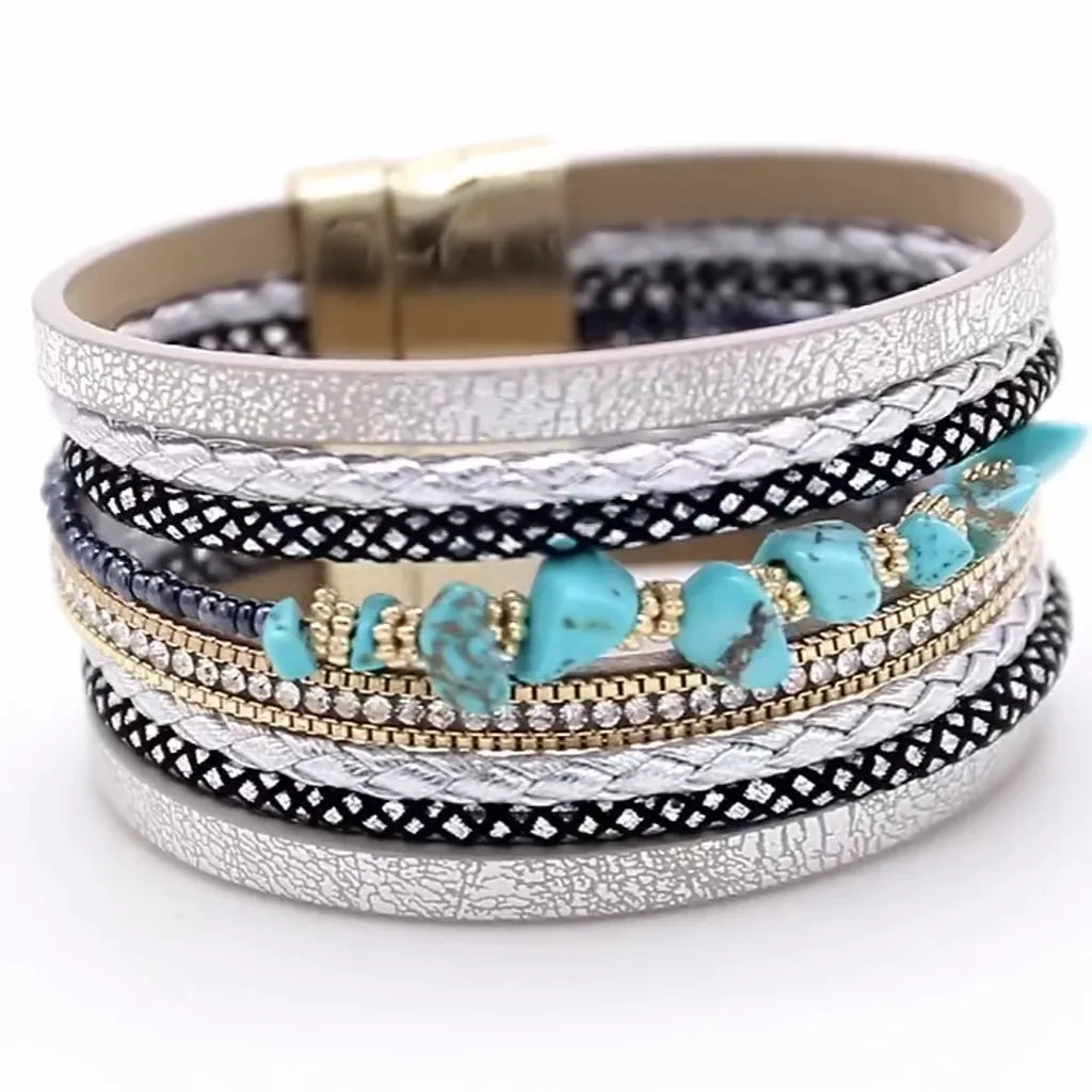 Gros plan des pierres turquoise et du cuir microfibre multi-rangs argenté, avec strass et chaînes dorées sur fond blanc.