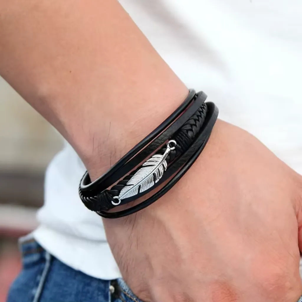 Gros plan sur le bracelet multi-rang Plume Liberté en cuir noir, porté au poignet d'un homme en tee-shirt blanc et jean bleu, vu de profil.