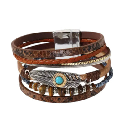 Bracelet Plume Quetzal multi-rangs en cuir microfibre marron sur fond blanc. Il est orné d'une breloque plume, de perles noires et de pierres assorties marron.