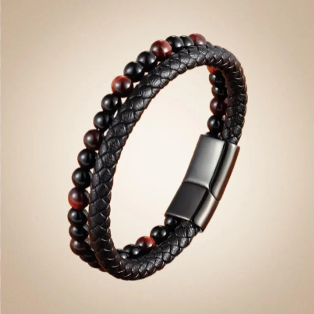 Bracelet double rang en cuir tressé noir, avec des perles d’œil de tigre jaune doré et d’onyx noire, soigneusement alignées pour un rendu épuré. Le bracelet est positionné en hauteur, mettant en avant ses détails de fabrication et son fermoir magnétique noir. Le fond dégradé du beige au blanc crée une ambiance lumineuse et élégante qui fait ressortir la richesse des matériaux.