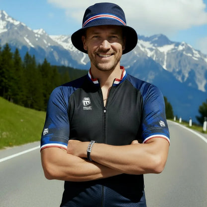 Plan poitrine action. L'homme souriant porte fièrement le bracelet Pulsar en cuir tressé noir. La chaîne de vélo en acier affirme la force du cyclisme sur la route des Alpes.
