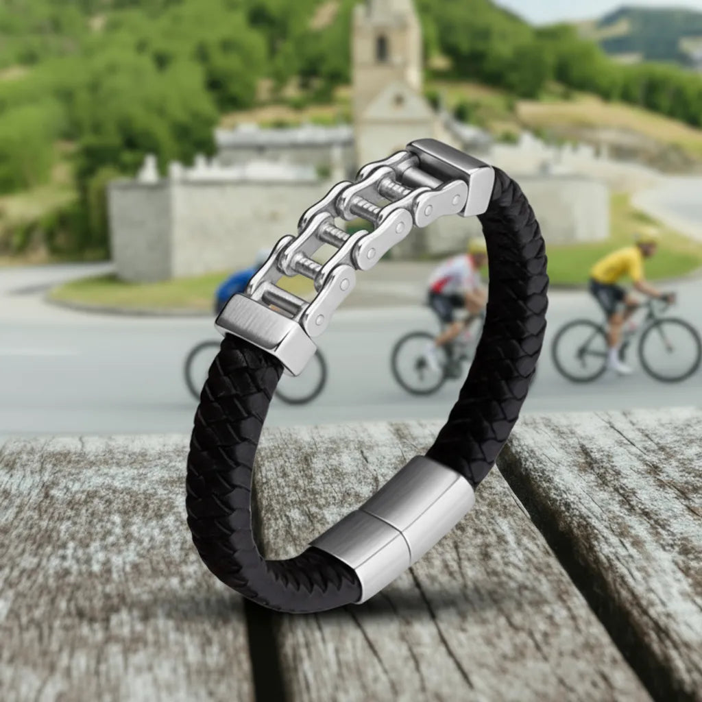 Contexte estival. Le bracelet Pulsar en équilibre, sa lanière tressée soulignant la robustesse de la chaîne de vélo en acier inoxydable, face au panorama de l'Alpe d'Huez.