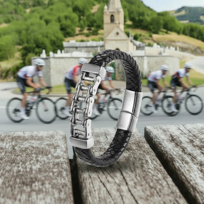 Ambiance cycliste. Le bracelet Pulsar cuir tressé noir dressé sur une table en bois, la chaîne de vélo face au col mythique de l'Alpe d'Huez. Force et endurance.