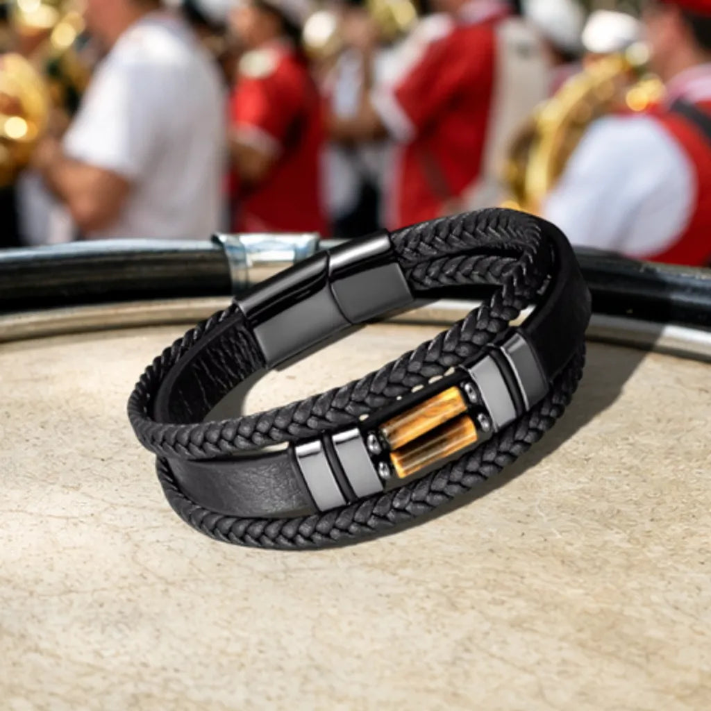 Le bracelet Solstice positionné sur le cercle métallique du tambour, illustrant l'harmonie entre l'acier noir du bijou et l'univers percutant d'une fanfare de prestige.