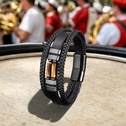 Le bracelet Solstice en équilibre sur la peau tendue d'un tambour, soulignant la souplesse de son cuir noir multi-rangs et l'éclat solaire des cylindres en oeil de tigre dans un décor de fanfare.