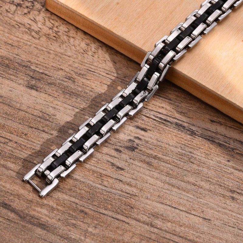 Bracelet Steel ouvert présenté à plat sur une table en bois - ses maillons et son fermoir sécurisé sont en acier inoxydable de qualité de couleur noir et argent - largeur 11 millimètres 