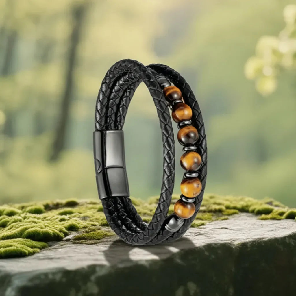 Photo de style du bracelet Talis, en équilibre sur un rocher. La triple épaisseur du cuir tressé noir magnifie la ligne centrale d'œil de tigre, symbolisant la force.