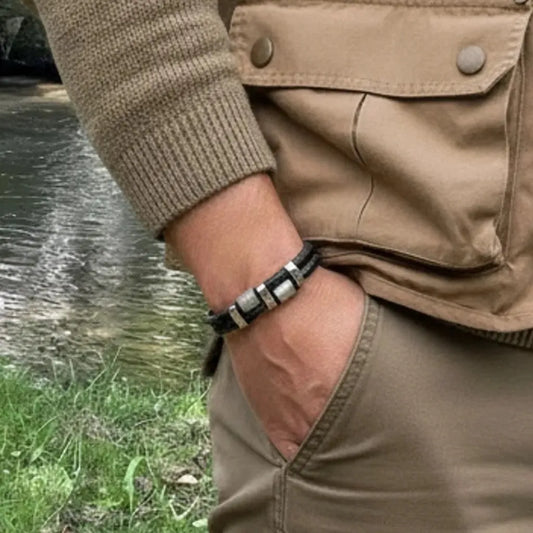Très gros plan grip. Le bracelet Talon à double cuir tressé noir et ses cylindres moletés portés sur une tenue de pêcheur. Symbole de la concentration au bord de la rivière à Nages.