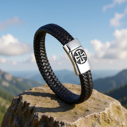 Bracelet Templiers dressé sur un rocher, vue du cuir tressé, fermoir et Croix Pattée sur fond montagneux avec ciel bleu nuageux.