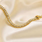 Bracelet tennis chaîne à maillon en acier inoxydable plaqué or avec rivière zircone cubique - bracelet chaîne pour femme posé ouvert à plat sur un tissus satiné de couleur blanc crème