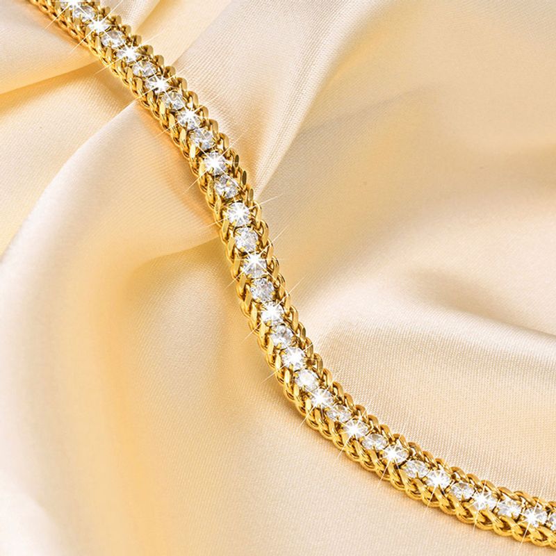 Bracelet tennis à maillons Miami en acier inoxydable plaqué or avec rivière zircone cubique - bracelet chaîne pour femme posé ouvert à plat sur un tissus satiné de couleur blanc crème 