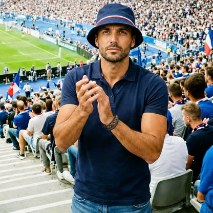 Homme en polo marine au Stade de France arborant le bracelet Vorg. Le cuir noir et l'éclat des perles oeil de tigre soulignent un style affirmé dans l'effervescence des tribunes.