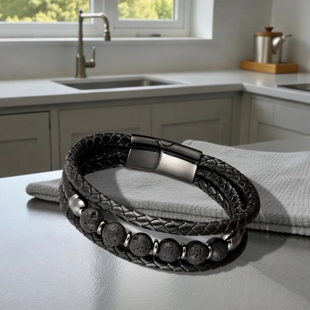 Composition élégante du bracelet Vulcan reposant en équilbre sur un torchon sur une table de cuisine, capturant les détails des perles de lave noire et la finition du fermoir devant une fenêtre ouverte.