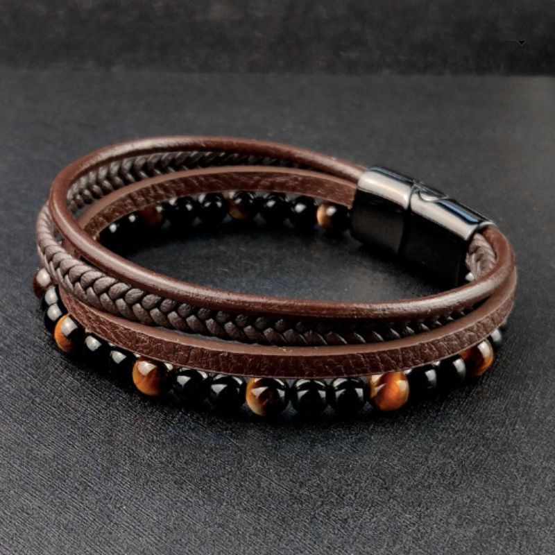 Bracelet cuir multilanière avec pierres naturelles agate noire et œil de tigre jaune pour homme, son fermoir magnétique en acier inoxydable est argenté – posé et fermé à plat sur un plan de travail gris foncé  – wrap cuir coloris marron.