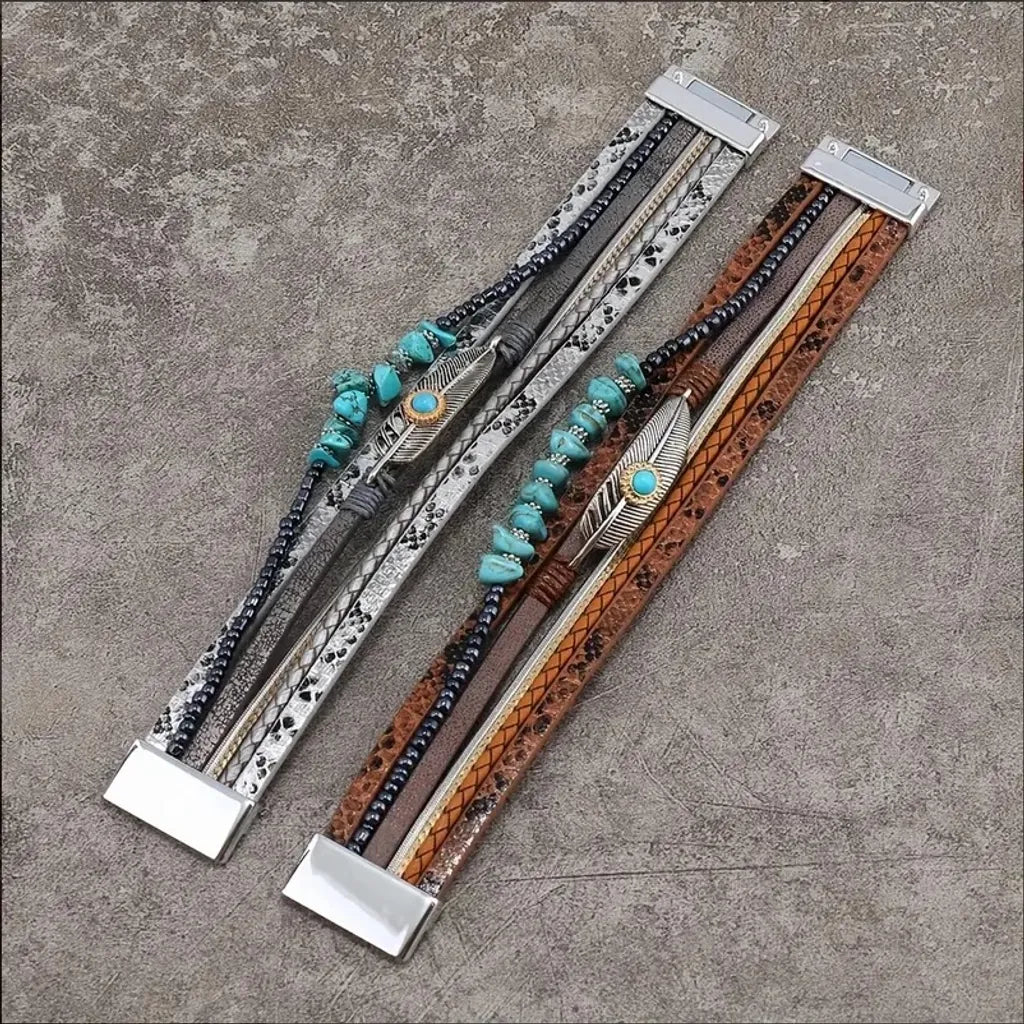 Deux bracelets Plume Quetzal en cuir microfibre, versions argenté et marron, photo à plat ; cabochon bleu, plume ajourée, fermoirs magnétiques.