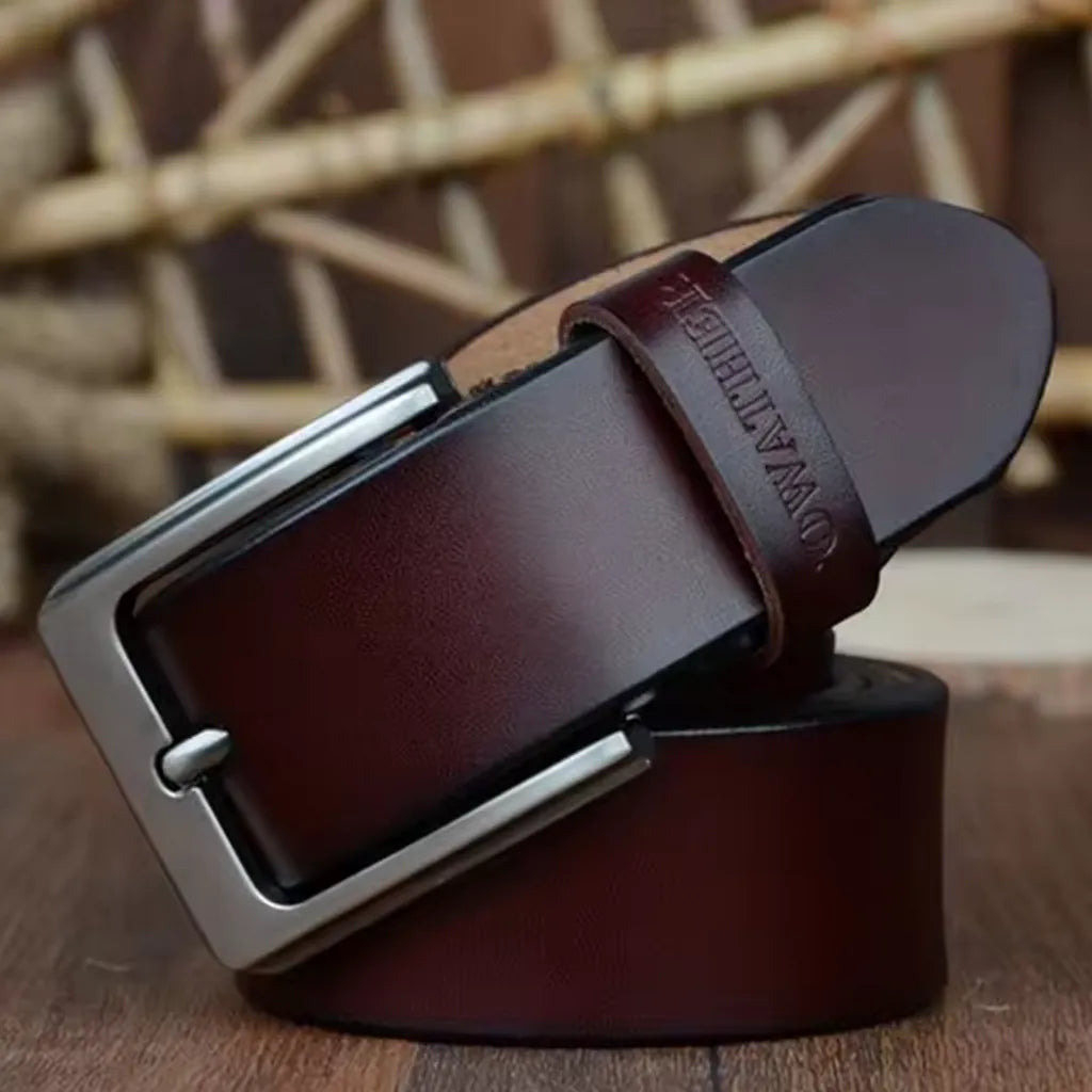 Ceinture pour homme en cuir véritable lisse, lanière en cuir de vache avec revêtement de protection. Sa boucle ardillon en métal est argentée et rectangulaire. Passant avec marque COWATHER gravé. Présentation fermée et enroulée sur les lames d'un parquet en bois. Coloris café.