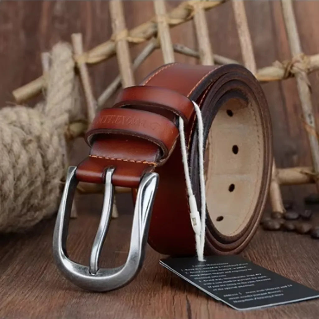 Ceinture pour homme en cuir de vachette lisse arborant une surpiqure décorative, avec revêtement de protection. Cette ceinture est présentée droite est enroulée, reposant sur sa boucle ardillon en métal argentée et arrondie. Passant avec marque COWATHER gravés. Présentation fermée et enroulée sur les lames d'un parquet en bois. Coloris cognac orangé.