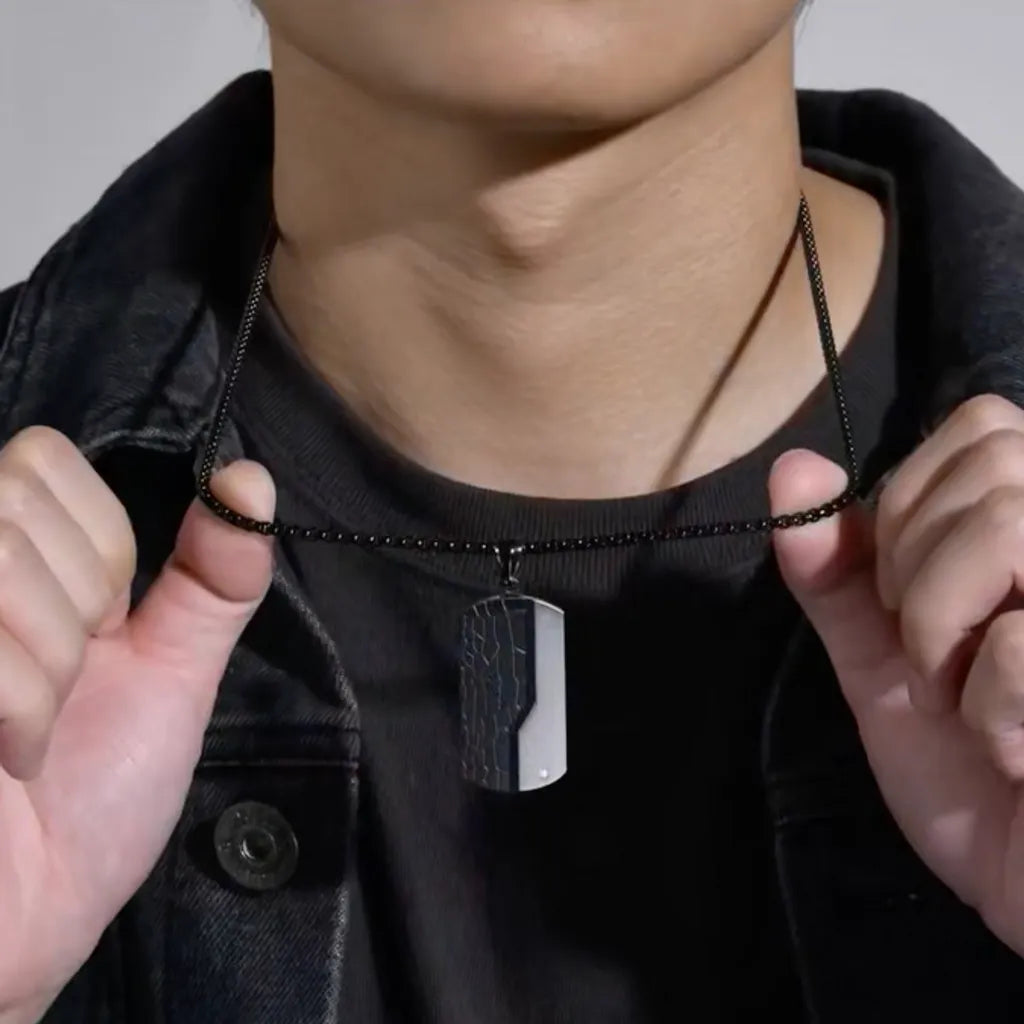 Ce collier avec pendentif style plaque rectangulaire est présenté autour du cou d'un homme vêtu d'un tee-shirt et d'un blouson en jean noir. Sa chaine à platine noire est en acier inoxydable, son pendentif rectangle est en fibre de carbone et en acier inoxydable – le petit plus est la Zircone cubique blanc qui brille sur le coin inférieur droit – Bijou pour homme.