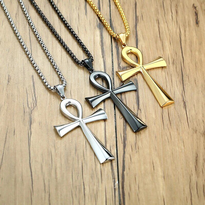 Trois colliers croix avec pendentif égyptien ankh présentés à plat sur une table en bois - bijoux en acier inoxydable pour homme - coloris - argent, noir ou or