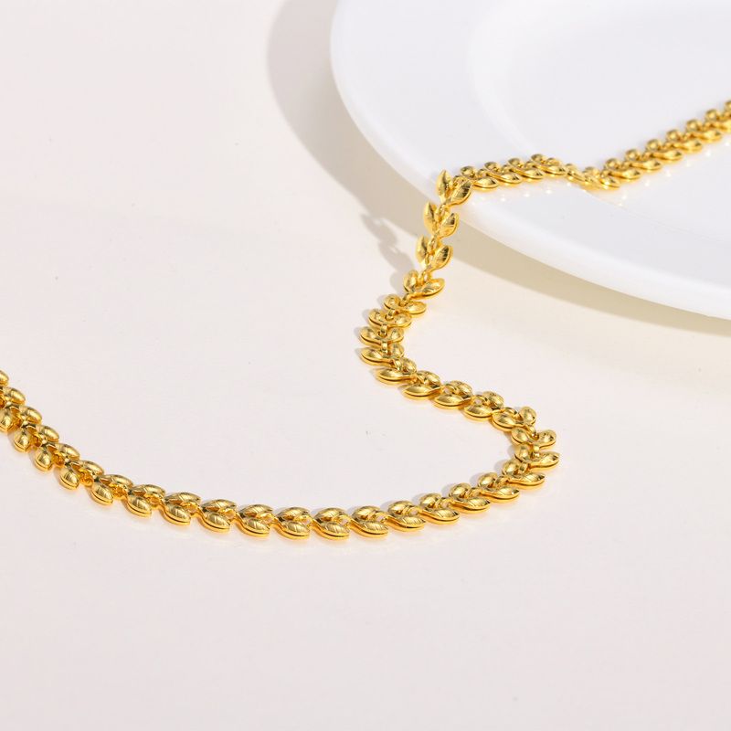Collier chaîne à maillons olives dorés en acier inoxydable pour femme - présenté ouvert tel un serpent posé sur une table blanche - coloris plaqué or