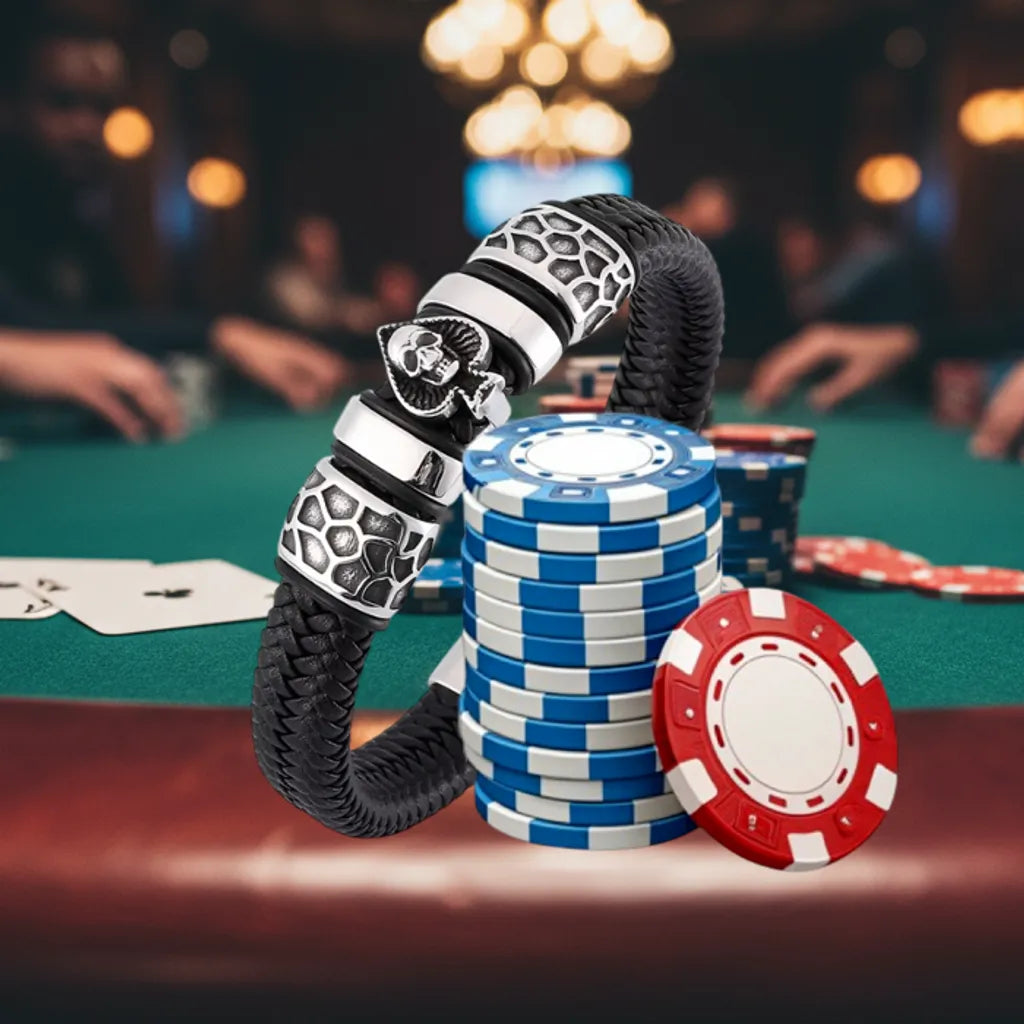Ambiance casino. Le bracelet Kaldor cuir tressé noir dressé, en équilibre contre une pile de jetons. Vue structurée du pique et de la tête de Mort.