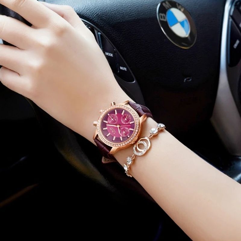 La Diana Cristal est une montre conçu pour les femmes élégantes, son cadran bordeaux est entouré d'une multitude de brillants, son boitier, ses index et ses aiguilles dorés et son bracelet en cuir bordeaux apporte une touche de sophistication - elle est portée autour d'un poignet d'une femme au volant d'une belle voiture de luxe.