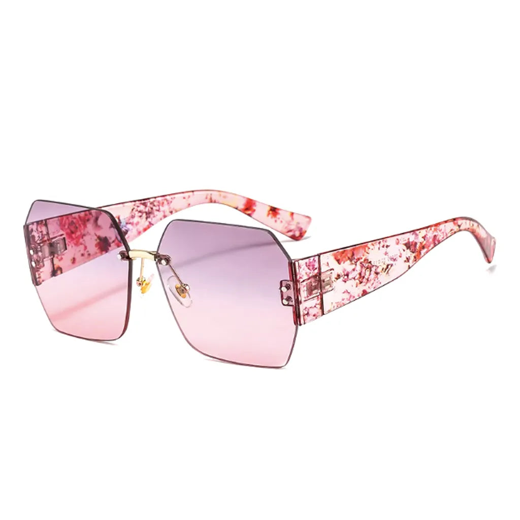 Lunettes de soleil carrées avec des verres roses dégradés et une monture unique ornée de motifs floraux sur les branches. Le cadre délicatement angulaire et les branches roses fleuries créent un style élégant et artistique, idéal pour un look estival sophistiqué.