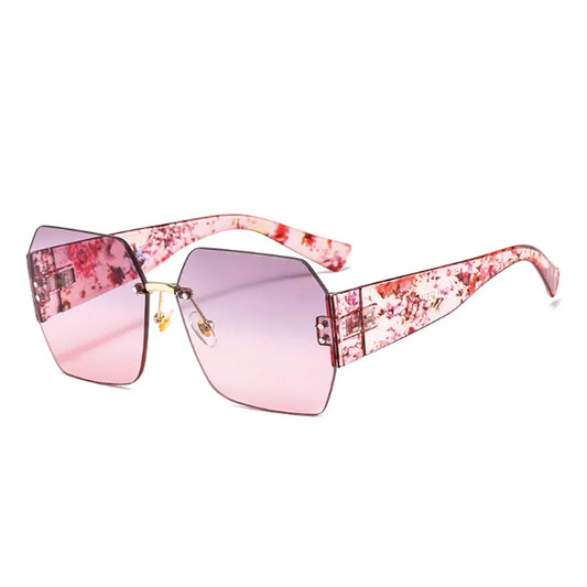 Lunettes de soleil carrées avec des verres roses dégradés et une monture unique ornée de motifs floraux sur les branches. Le cadre délicatement angulaire et les branches roses fleuries créent un style élégant et artistique, idéal pour un look estival sophistiqué.