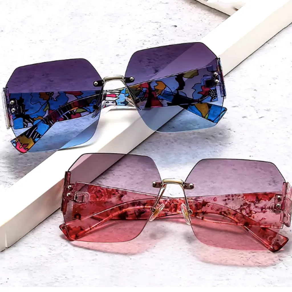 Deux paires de lunettes de soleil géométriques avec des verres dégradés en mauve et rose, posées l'une devant l'autre. La paire arrière arbore une monture colorée avec motifs abstraits, tandis que la paire avant présente des motifs floraux roses, offrant un style unique et audacieux.