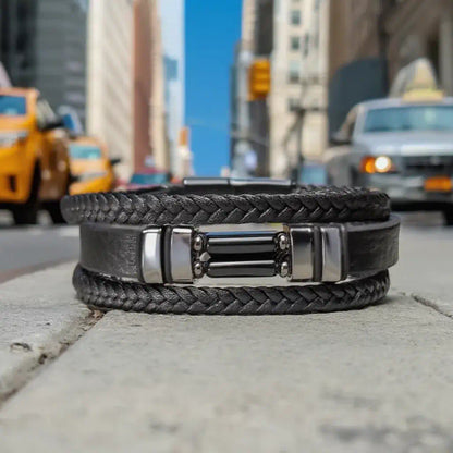 Vue frontale du bijou Éclipse reposant à plat sur le trottoir, où le contraste entre le cuir noir souple et le décor minéral de la ville souligne le design totémique et moderne de cette pièce multi-rangs.